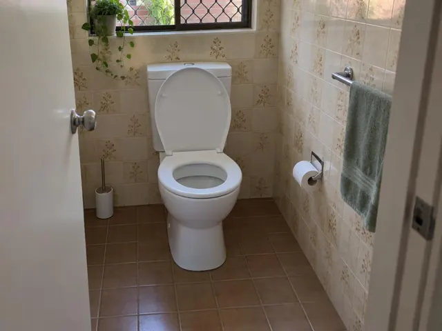 Clean white toilet in a tiled bathroom with a towel rail and window in Winston Hills