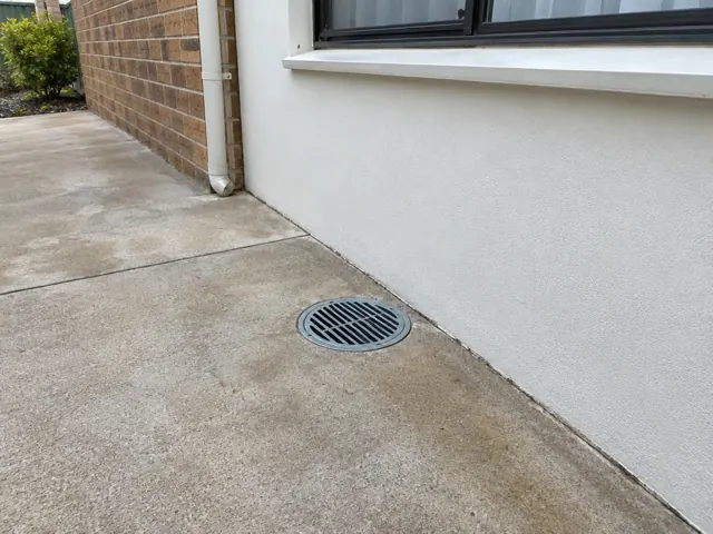 Dry outdoor gully grate beside a white wall and brick house exterior in Toongabbie